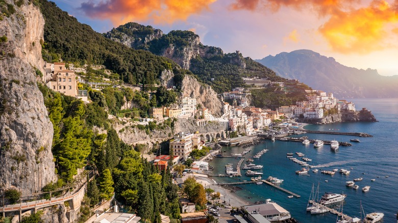 Coastal town with marina and lush, rocky hillside.