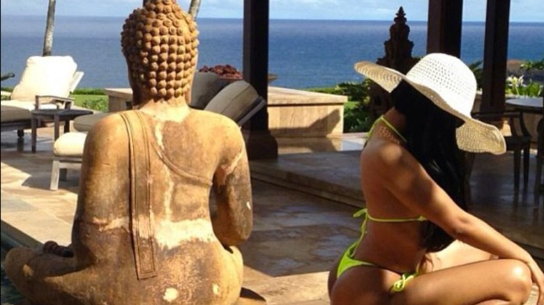 Nicki Minaj posing in a bikini with her back turned to a Buddha statue