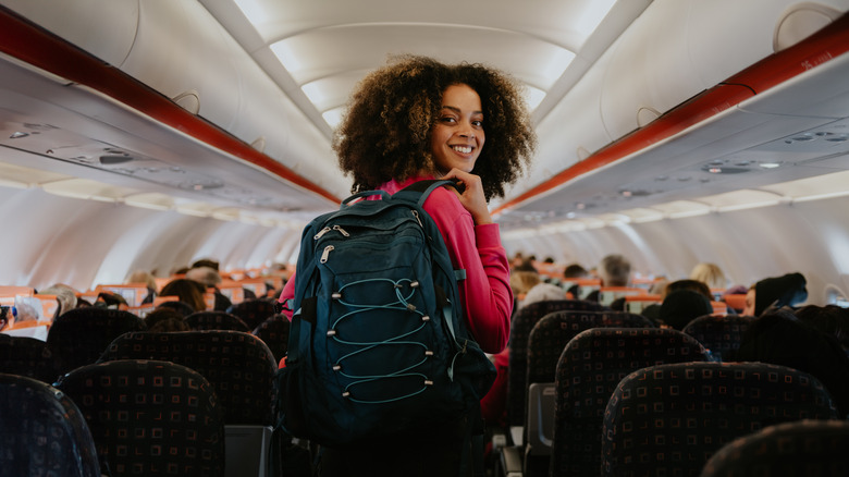 smiling woman holding backpack on plane