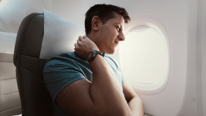 man on plane grimacing and touching neck