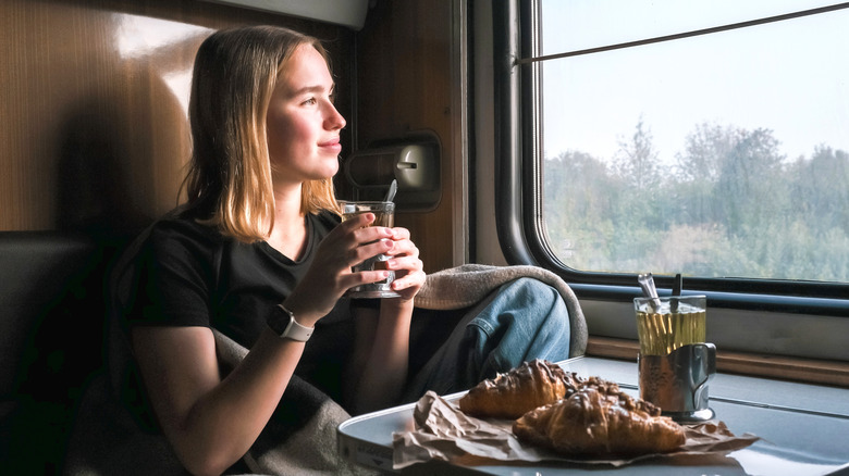 A solo traveler looks out of the train window while sipping tea