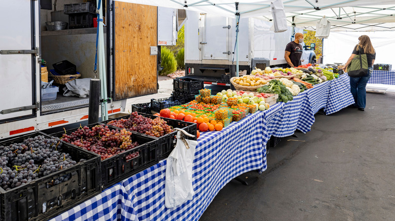 Long table at farmers market loaded with fresh grapes, green vegetables for sale