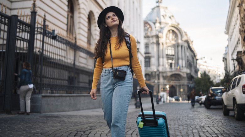 Solo female traveler walking with rolling luggage through a city