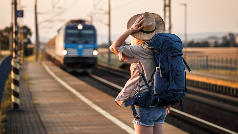 Backpacker holds onto her hat as a train passes through a station