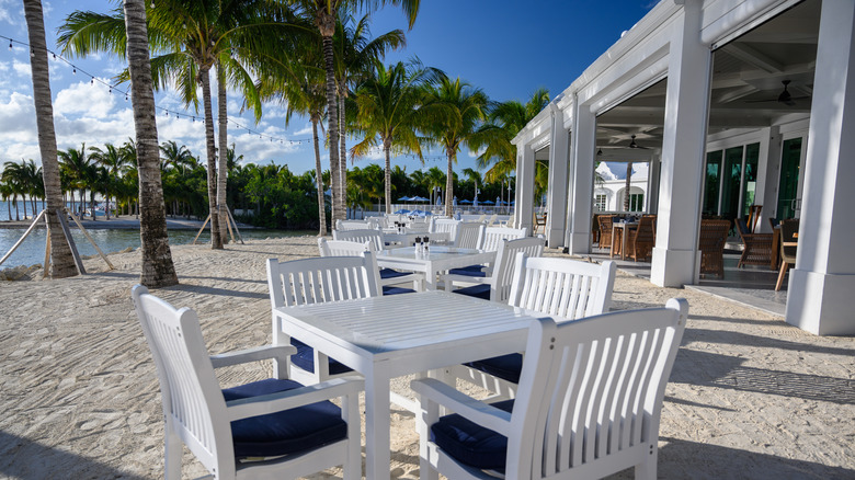 Outdoor dining area on the sand with palm trees and patio on the right at Isla Bella Beach Resort in the Florida Keys.