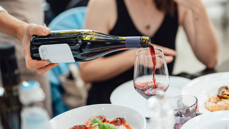 A man pouring red wine for a woman at a dining table.