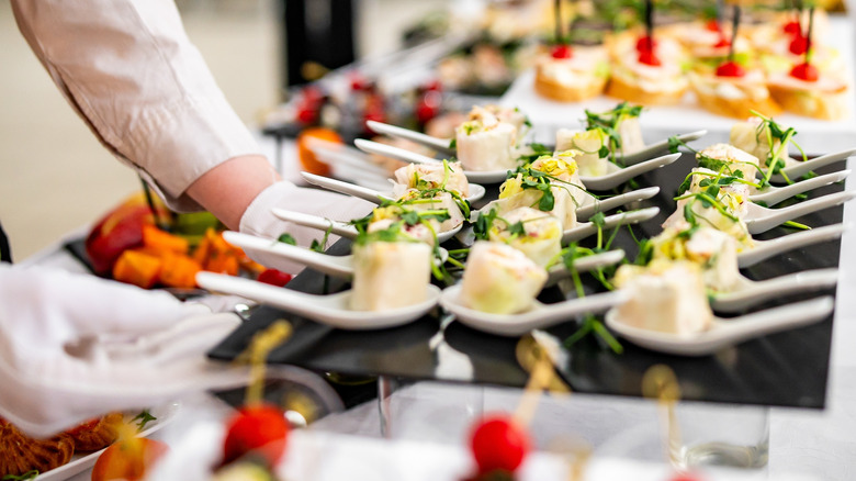 A chef putting out gorumet appetizers on a buffet.