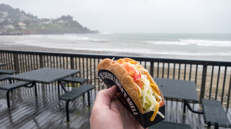 A Taco Bell customer holds up his order in front of the beach view.