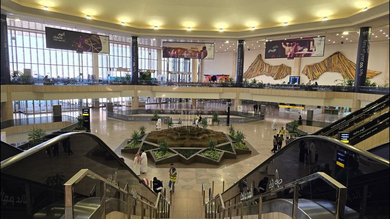 between two escalators looking down at a plant feature inside King Fahd International Airport