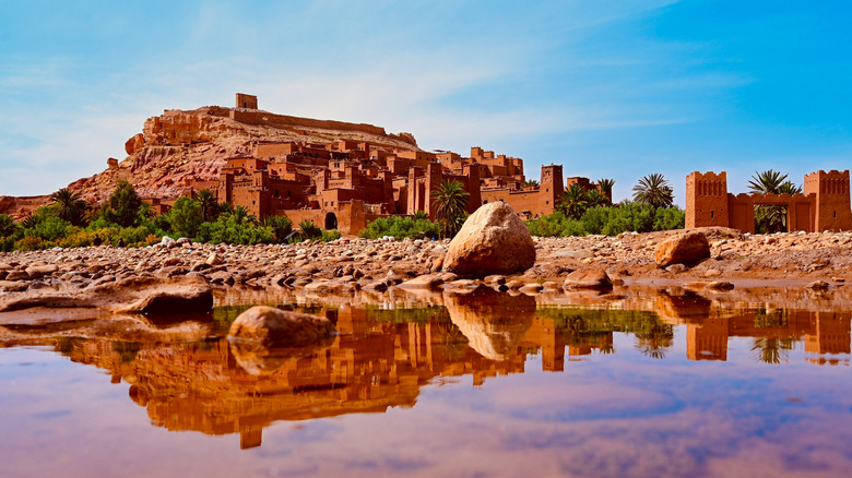 Clay walls of Ourzazate reflected in water from oasis