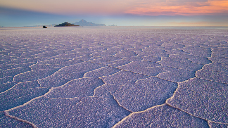 Crusted polygonal-shaped salt plates linked together forming a huge expanse with clouds and hills in the distance during sunset