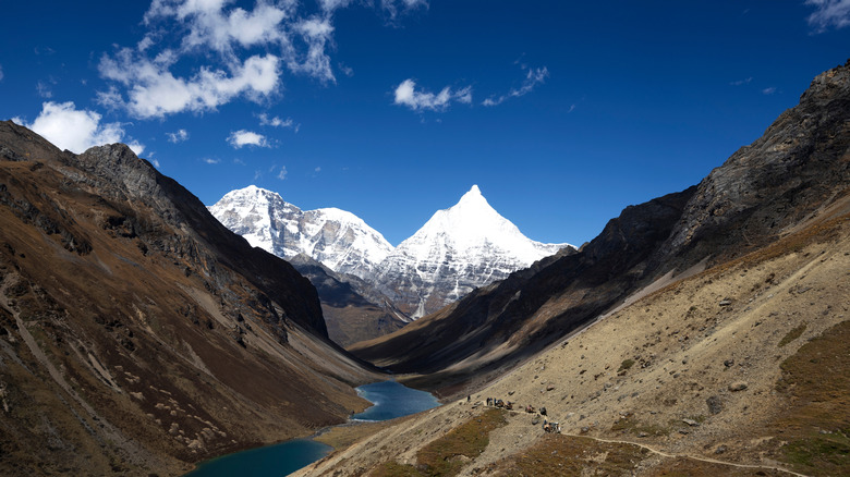 Brown rocky hills slope down to an alpine lake with towering snowy peaks in the distance in Bhutan