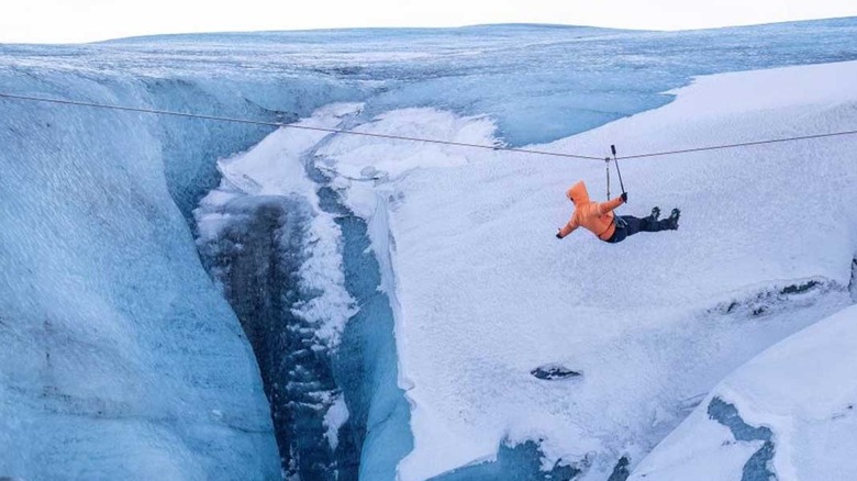 a person in a yellow coat flies over a glazier on a zip line