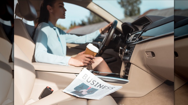 Woman drives car holding coffee cup.