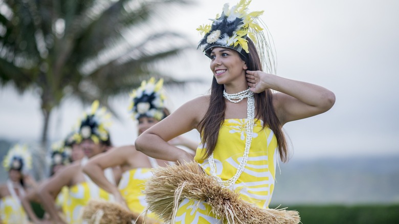 Girls dressed in yellow with floral head dresses dancing.