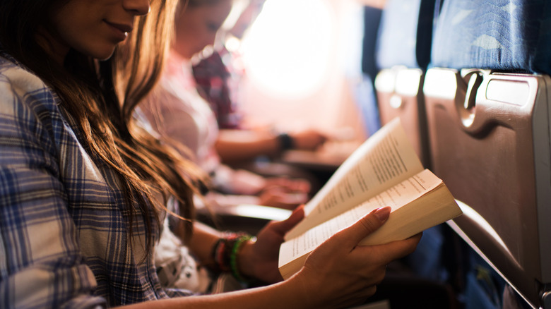 Person reading book aboard airplane