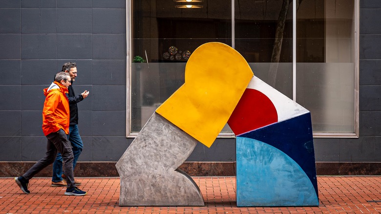 two men walk past sculpture