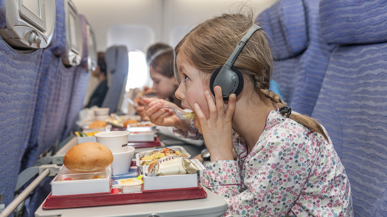 Girl on plane with headphones, eating