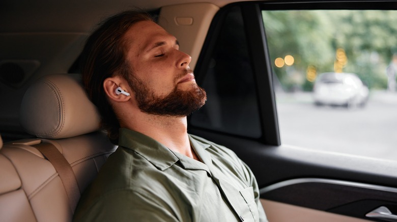 Sleeping man wearing earbuds in the back of a car.