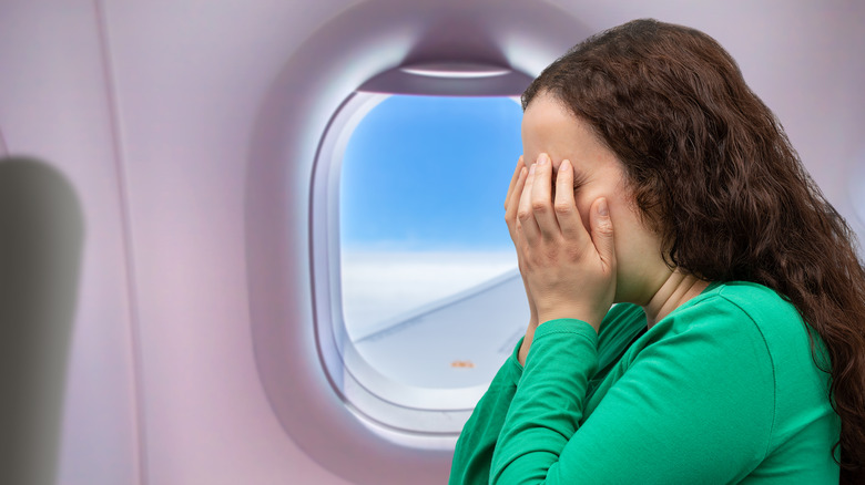 An anxious person covering her face mid-flight