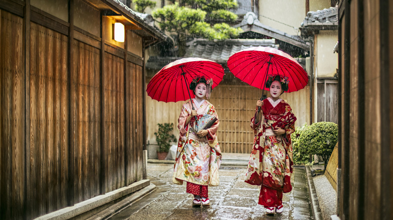 Two women in traditional japanese kimono carrying red umbrellas in an alley