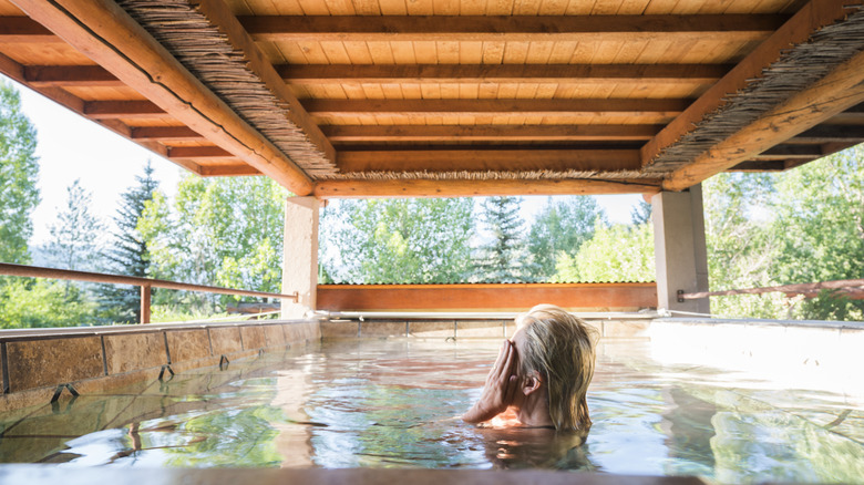 Woman bathing alone in hot spring pool with cedar roof