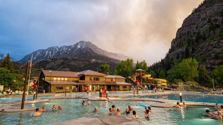 Bathers at hot springs resort with water slides framed by mountains