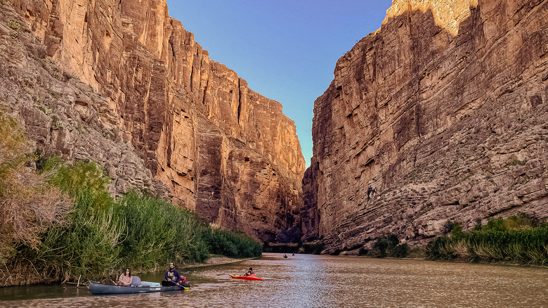 People kayaking in river between cliffs