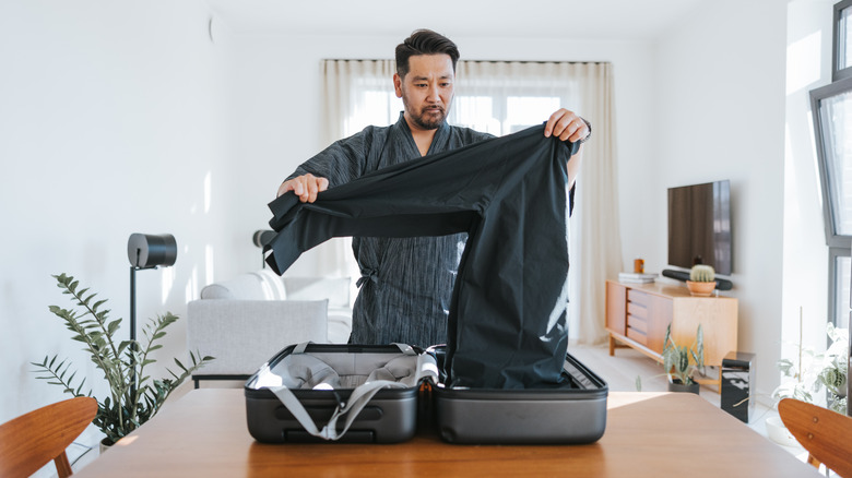 Man folding shirt into suitcase