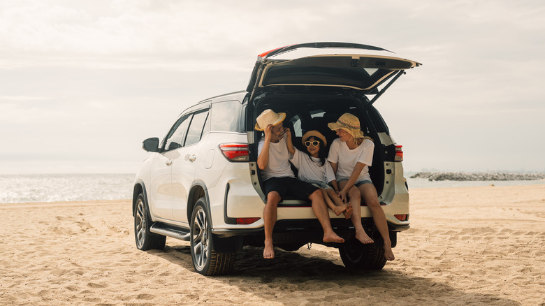 A family sits in a car in front of a beach