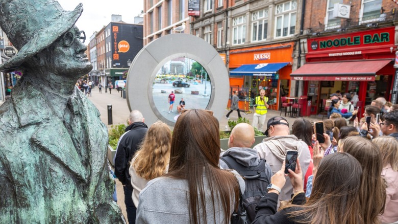 People gather in front of the Dublin Portal sculpture, which is located beside a statue of James Joyce