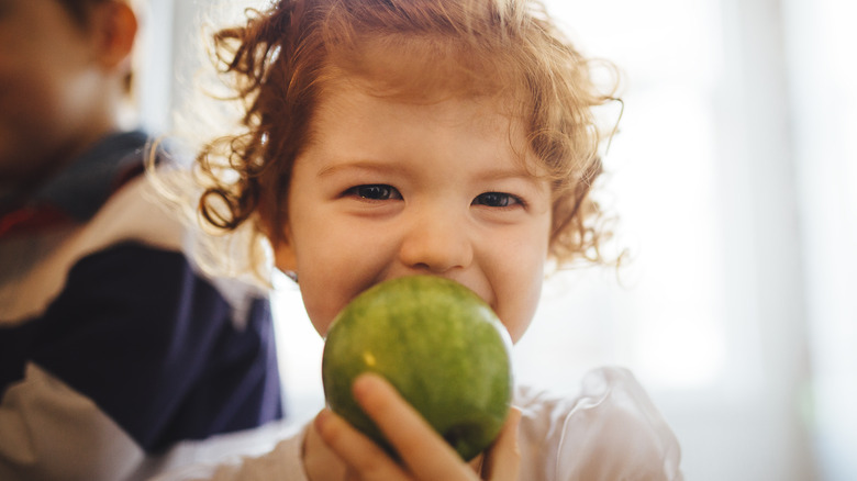 little child eating green apple