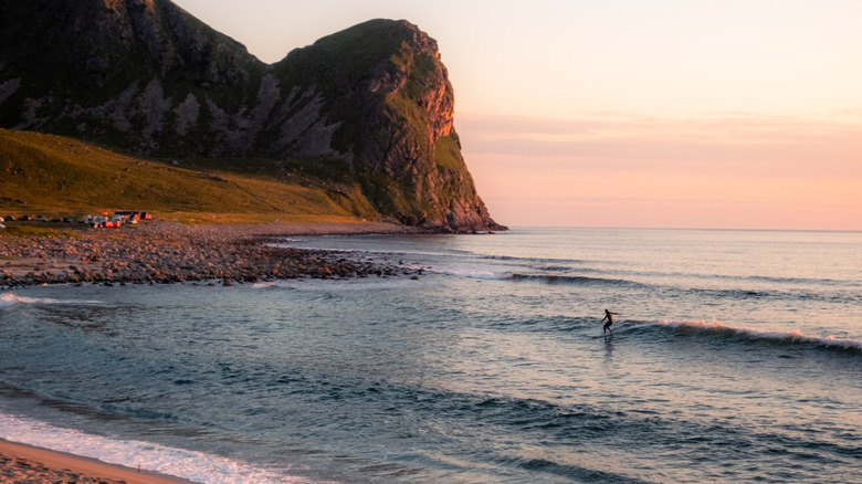 Lone surfer catches a wave at sunset in the waters off Norway's Lofoten archipelago