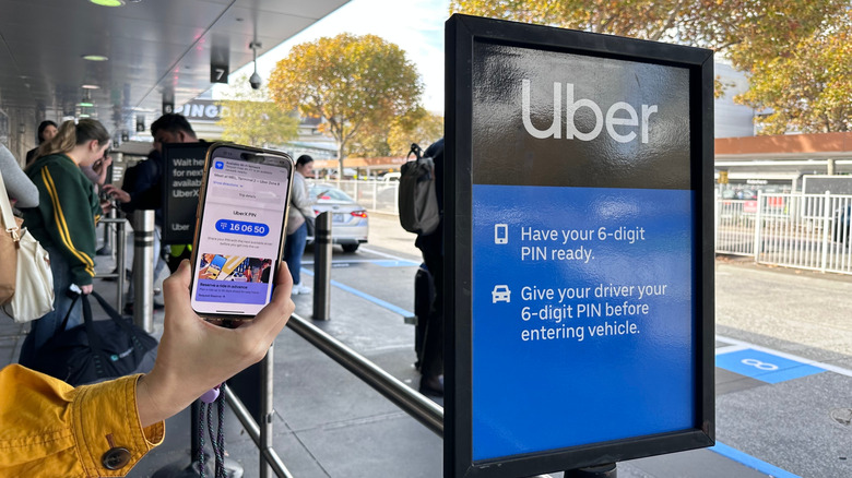 Woman holds up Uber pin code next to sign at airport