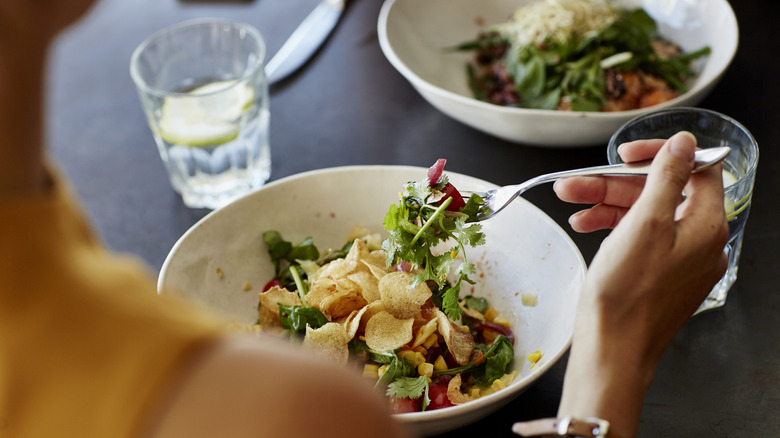 Someone eating a salad and drinking water with lemon