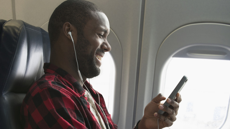 Man wearing plaid shirt while looking at his phone on airplane