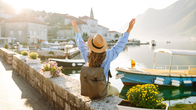 Woman from behind sitting on wall raising arms as she looks at European city