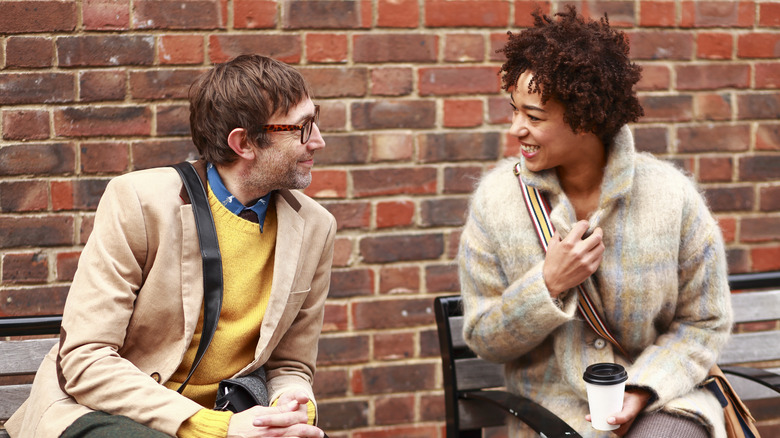 Man and woman sitting on benches against brick wall in a conversation