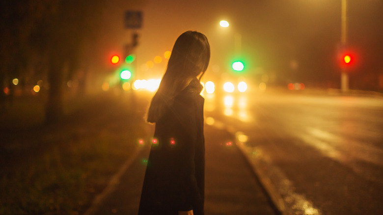 Lone woman with back to camera crosses street at night