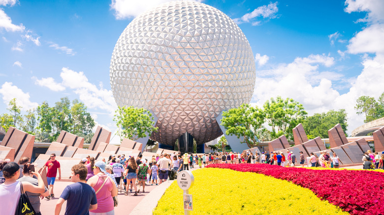 EPCOT's  Spaceship Earth surrounded by crowds against a bright blue sky full of fluffy white clouds