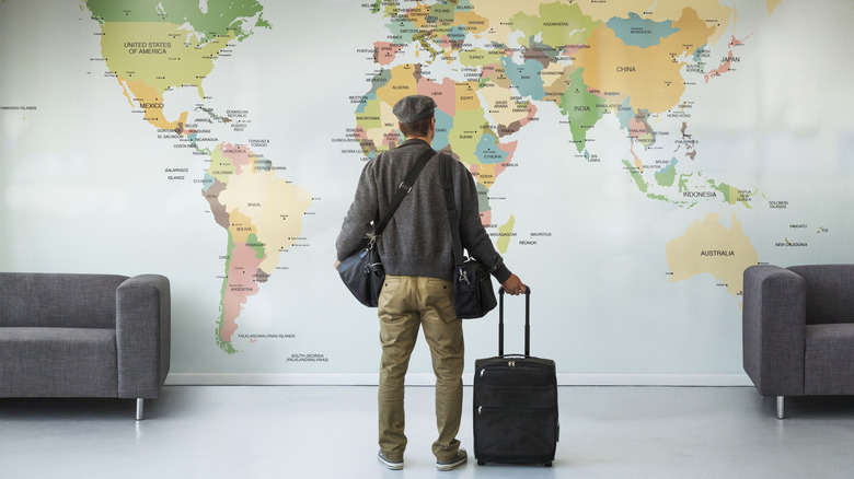 Man with luggage standing in front of world map