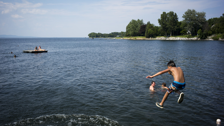 People swimming and diving into a lake with a raft out on the water