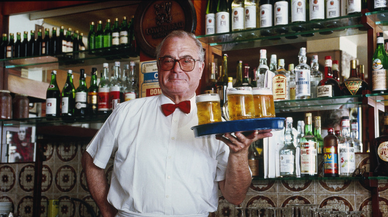 Italian barman holds tray of beers behind bar