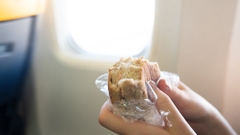 A pair of hands holds up a sandwich on an airplane.