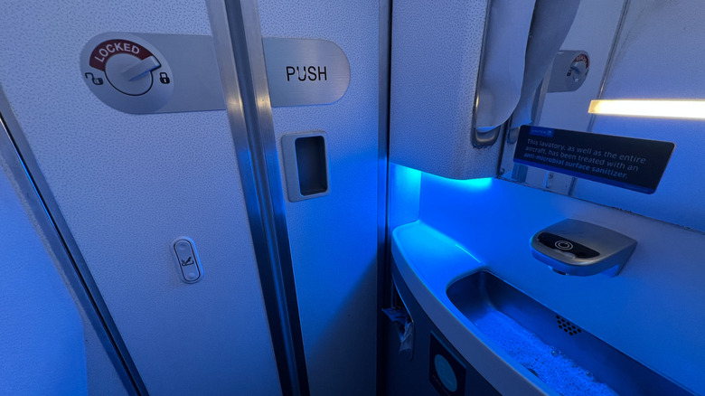 An interior view of an airplane bathroom, featuring a red locking indicator on the door.