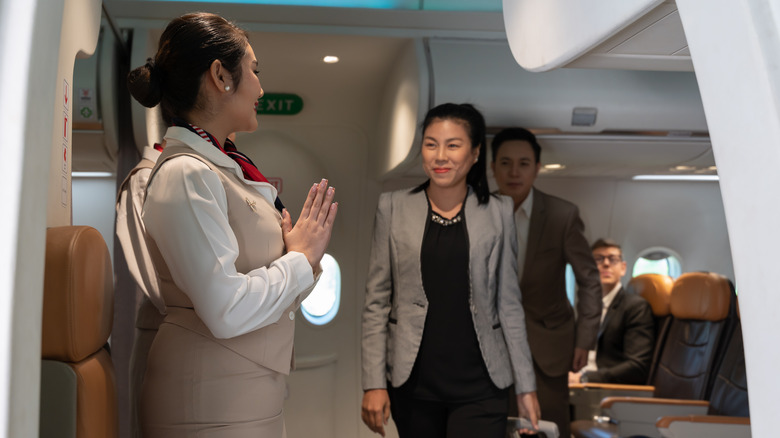 Flight attendant welcoming passengers on plane