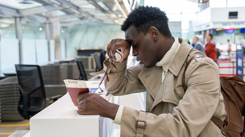 An upset man at an airport, holding his passport and boarding pass