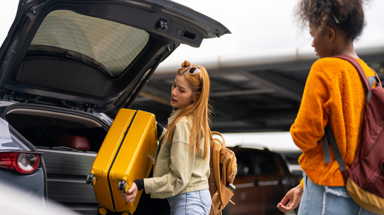 Two travelers take their luggage out of the car