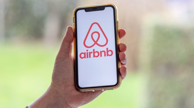 A person holding a smartphone with the Airbnb logo on the screen