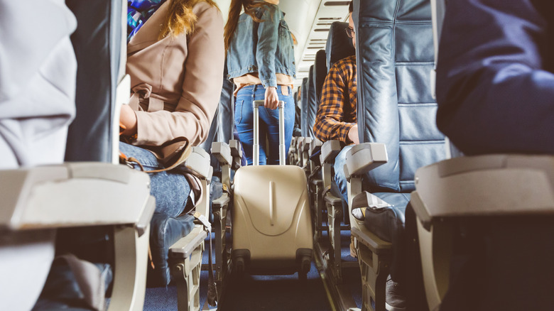 Person pulling wheeled luggage down airplane aisle